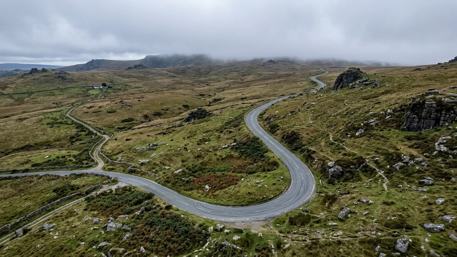 A road climbing onto the northern edge of Dartmoor past granite outcrops and open moorland with cloud on the high ground